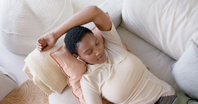 Woman relaxing on a couch with headphones, enjoying music. She looks serene and comfortable. Ideal for themes related to relaxation, leisure, music enjoyment, and self-care.