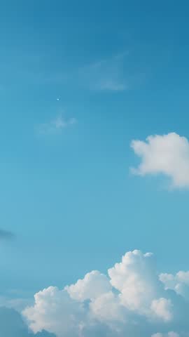 Vertical footage showing drifting cumulus clouds crossing blue sky with tiny aerial speck