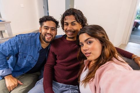 Multiethnic friends taking selfie on cozy living room couch, smiling and relaxed
