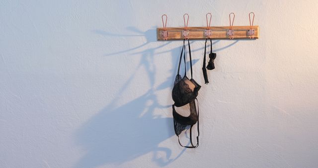 A black bra hangs from a wooden coat rack on a white wall, with copy space. The simplicity of the scene suggests a focus on minimalism or the concept of decluttering.