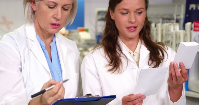 Female pharmacists in white lab coats reviewing medication and discussing notes in a pharmacy. Ideal for use in healthcare, pharmacy, teamwork, and pharmaceutical product contexts.