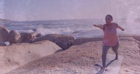Woman practicing yoga on rocky coast at sunrise, balancing pose with ocean waves, mindful practice