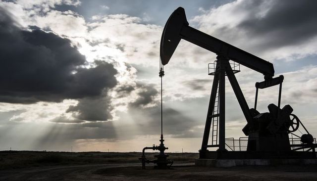 Oil pumpjack silhouette under dramatic sun rays over empty prairie well site at dusk