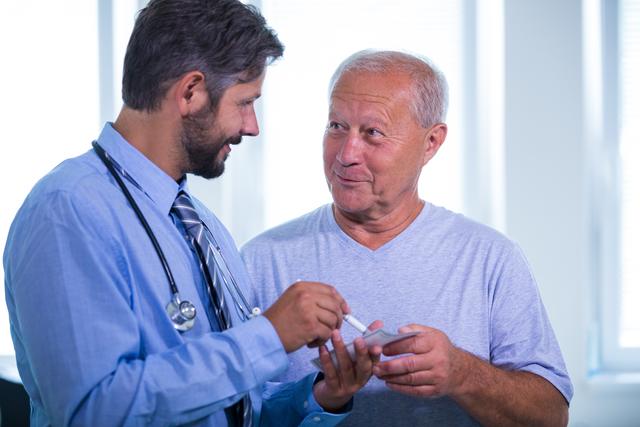 Senior patient consulting with a doctor in a hospital setting. The doctor is holding a medical device and explaining something to the patient. This image can be used for healthcare websites, medical blogs, patient care brochures, and health-related articles to illustrate doctor-patient interactions and medical consultations.
