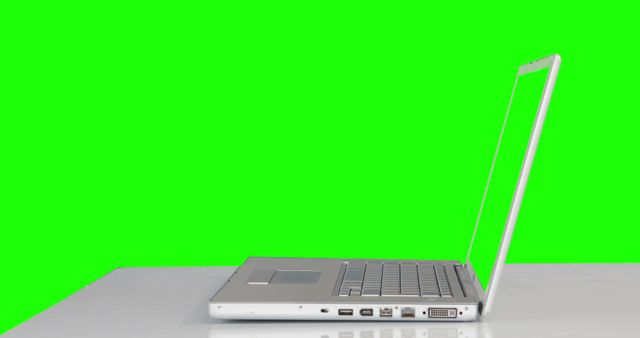 A silver laptop is open at a 90-degree angle on a bright green background, with copy space. The vibrant green backdrop provides a stark contrast that accentuates the sleek design of the modern laptop.