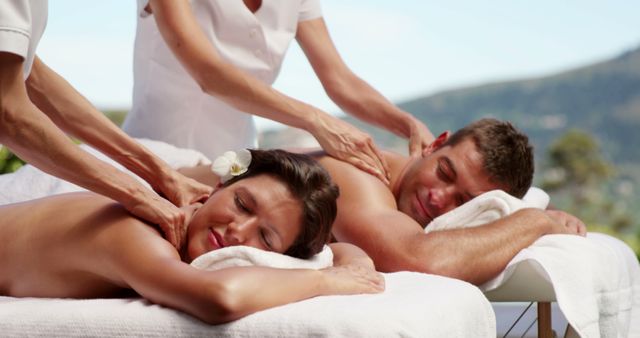 Couple receiving a relaxing massage outdoors at a luxurious spa resort, creating a calming and serene atmosphere. Suitable for advertisements and promotions related to wellness, spa resorts, relaxation, pampering services, and romantic getaways.