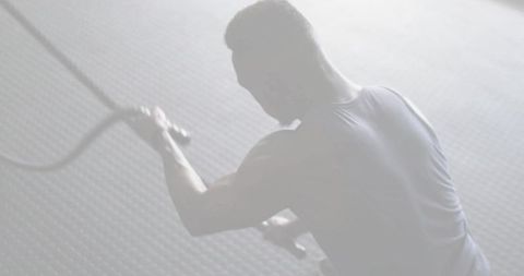 Backlit african american athlete swinging battle ropes in high-intensity gym workout