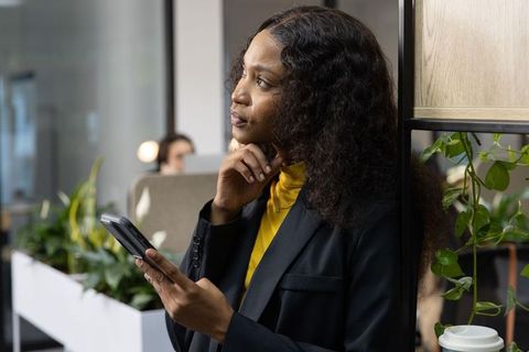 Contemplating african american professional leaning in modern office holding smartphone