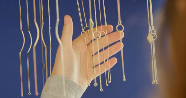 A person is reaching out to delicate hanging necklaces, choosing one to wear or admire. Jewelry displays like this often invite the viewer to appreciate the craftsmanship and design of each piece.