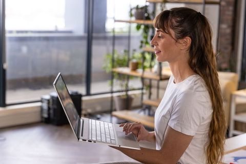 Young Woman Smiling While Using Laptop in Bright Modern Office