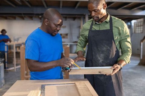 African american carpenters measuring and marking plank collaborating on cabinet
