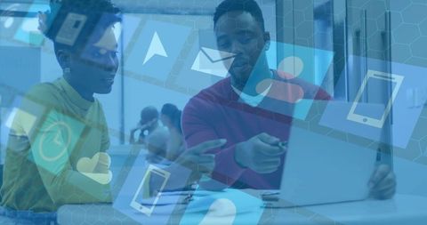 Collaborating on laptop with digital icons overlay in modern coworking workspace