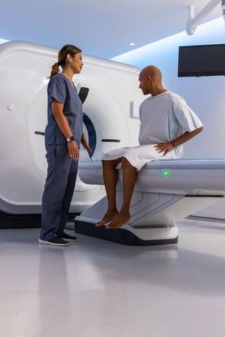 African american male patient consulting technologist at ct scanner in radiology suite