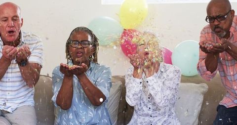 Joyful Senior Friends Blowing Confetti in Living Room Celebration