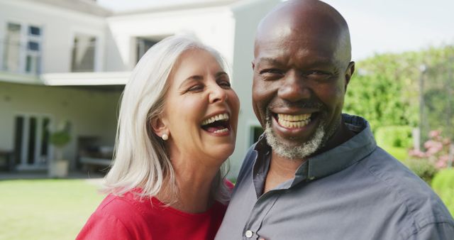 Senior couple enjoying a moment outside in a beautiful garden, both smiling and laughing heartily. Ideal for marketing retirement communities, lifestyle blogs, and any content promoting happiness and relationships in later life.