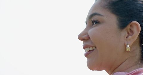 Smiling woman in profile looking upward wearing gold teardrop earring and pastel top