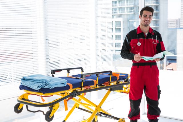 Portrait of handsome paramedic with medical report standing besides a stretcher