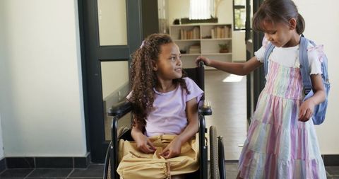 African american teen girls chatting in school hallway, one using wheelchair, showing inclusion