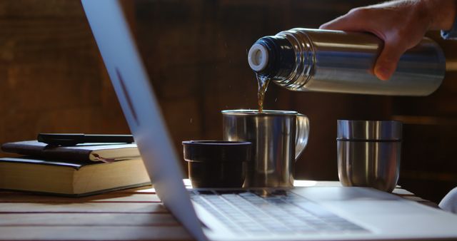 Person Pouring Hot Drink from Thermos beside Laptop - Download Free Stock Images Pikwizard.com