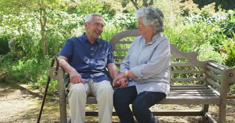 Happy Senior Couple Holding Hands on Garden Bench