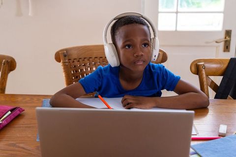 African american boy studying at home table with headphones and laptop for remote learning