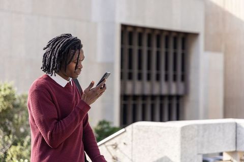 Young man standing and speaking into smartphone outside modern concrete building