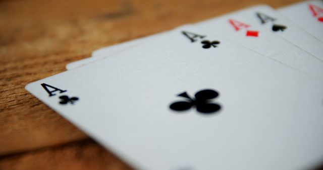 Close-up view of a set of playing cards showing four aces from different suits on a wooden table. Ideal for use in themes involving gambling, luck, excitement, and poker games. Useful for advertising casinos, card game tutorials, and game night promotions.