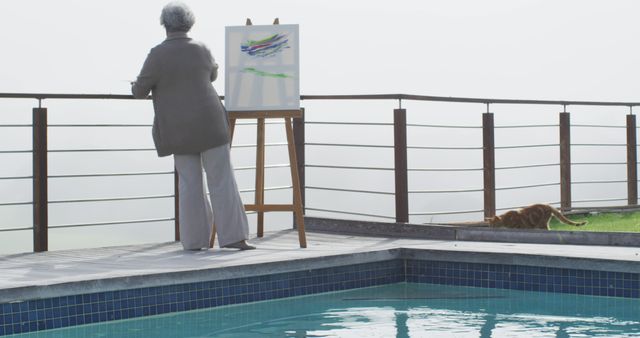 Rear view of african american senior woman painting on canvas by the pool in the balcony at home. retirement senior lifestyle living in quarantine lockdown concept