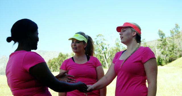 Three women are engaging in outdoor exercise activities. They are wearing matching pink shirts and exploring the natural surroundings. This image can be used for advertisements or campaigns promoting fitness community, team building, unity in sports, and healthy living.