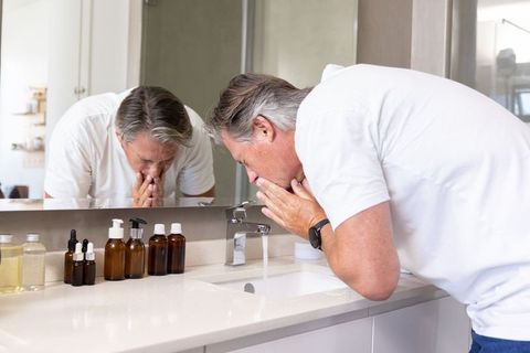 Senior man washing face at bathroom sink during morning grooming routine and self-care