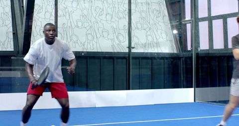 Players Competing on Blue Padel Court with Glass Walls and Mural