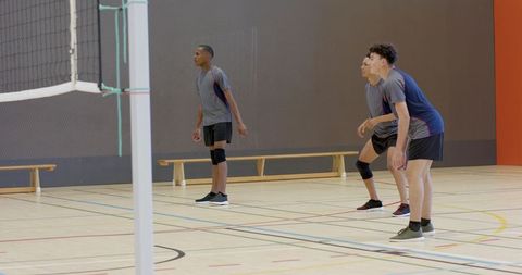 Diverse male volleyball teammates standing ready near net on indoor gym court
