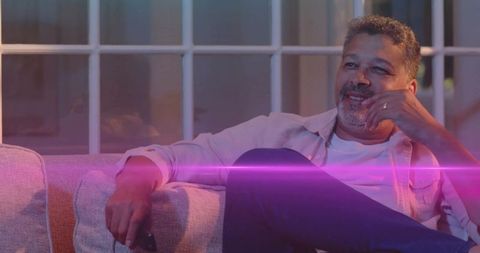 Smiling man relaxing on sofa holding remote showing ring warm living room lighting