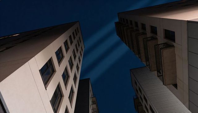 Converging high-rise towers at night with stacked balconies and dramatic sky beams
