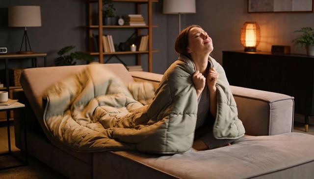 Woman wrapping in quilted blanket on sectional sofa relaxing in cozy living room