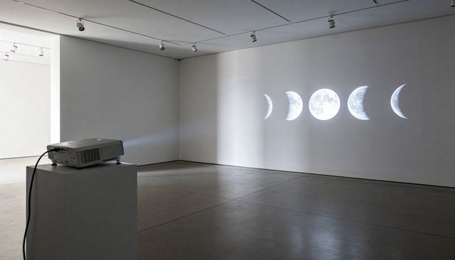 Projecting lunar phases on minimalist gallery wall with digital projector and pedestal