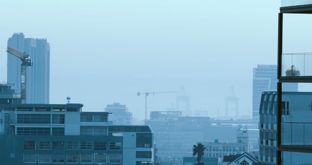 Urban skyline at dawn featuring construction cranes in misty blue light. Suitable for illustrating real estate development, urban growth, architectural themes, and city planning. Can be used in presentations about urbanization, articles discussing construction trends, or as a background for city-themed designs.