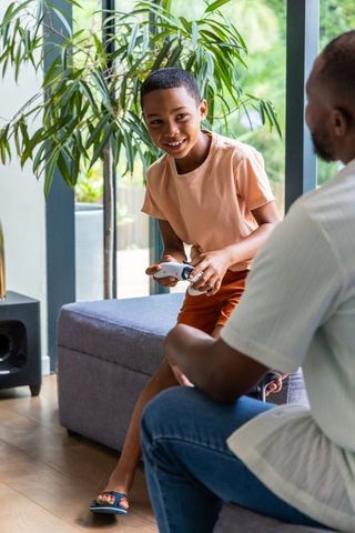 African american father and son playing video game together in sunlit living room