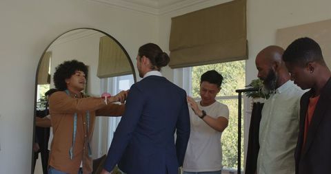 Groom with friends adjusting suit before wedding ceremony
