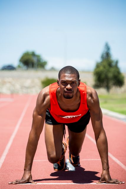 This image captures a determined athlete in a starting position on a running track, ready to sprint. Ideal for use in sports-related content, fitness promotions, motivational materials, and athletic training guides. Perfect for illustrating themes of determination, preparation, and competitive spirit.