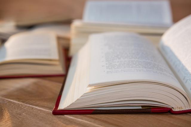 This image shows a close-up view of several open books on a wooden table, emphasizing the pages and text. Ideal for use in educational materials, library promotions, study guides, and articles about literature and learning. It conveys a sense of academic dedication and the pursuit of knowledge.