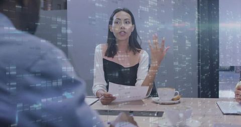 Female leader presenting in modern boardroom holding papers and gesturing during team meeting