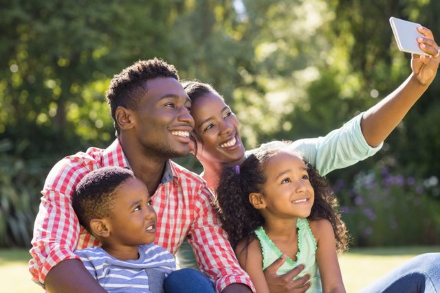 African American family enjoying time together in a park, capturing a joyful moment with a selfie. Perfect for advertisements, family-oriented campaigns, or articles about family bonding and outdoor activities.
