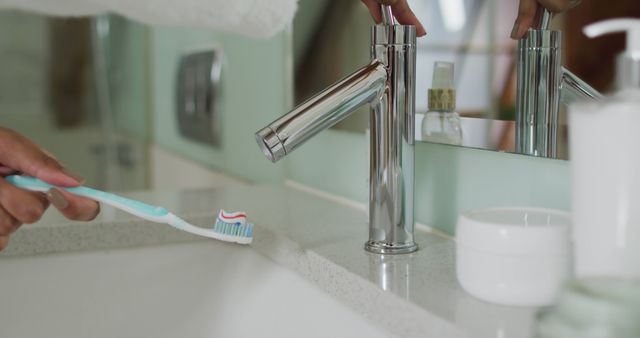 Depicting personal hygiene, this view focuses on a person preparing a toothbrush with toothpaste by a bathroom sink. Useful for illustrating topics on dental hygiene, morning routines, health, and daily self-care activities. Ideal for use in healthcare brochures, wellness blogs, and lifestyle magazines.