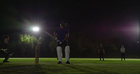 Batsman standing at crease under floodlights preparing to bat during night cricket match