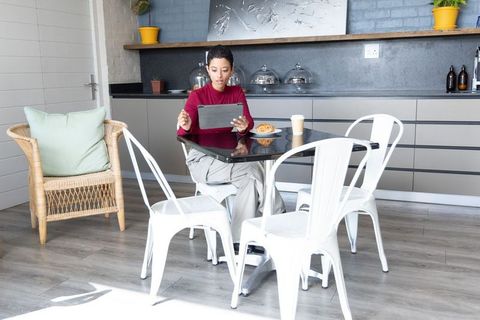 African american woman working on tablet in sunlit bright kitchen with pastry and coffee