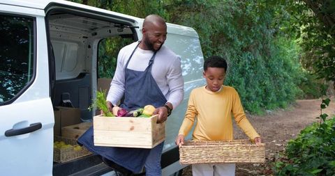 African american farmer and son loading fresh harvest into baskets by delivery van