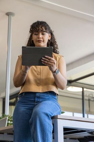 Young woman using tablet while sitting on high bench in modern coworking workspace