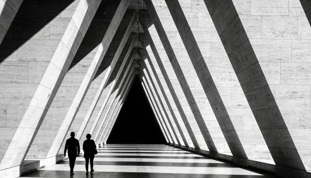 Silhouetted Pair Walking Through Triangular Colonnade Casting Dramatic Diagonal Shadows