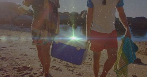 Friends carrying cooler on sunset beach walk